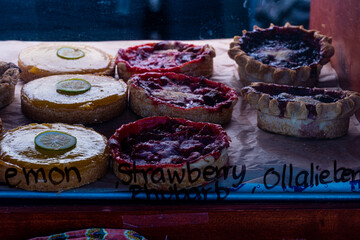 lemon and berry tartlets in rows inside display case with handwritten labels on glass at local farmer's market