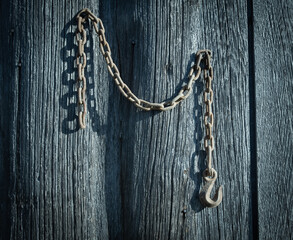 A rusty old farm tractor chain with a hook hangs from a barn board pine shed