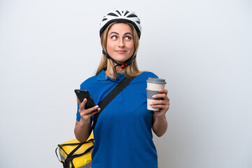 Young caucasian woman with thermal backpack isolated on white background holding coffee to take away and a mobile while thinking something