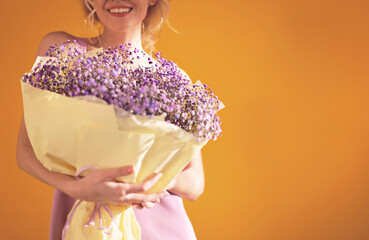 Studio portrait of young beautiful woman with bunch of purple flowers on yellow background. Gypsophila. Spring.