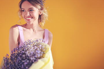 Studio portrait of young beautiful woman with bunch of purple flowers on yellow background. Gypsophila. Spring.