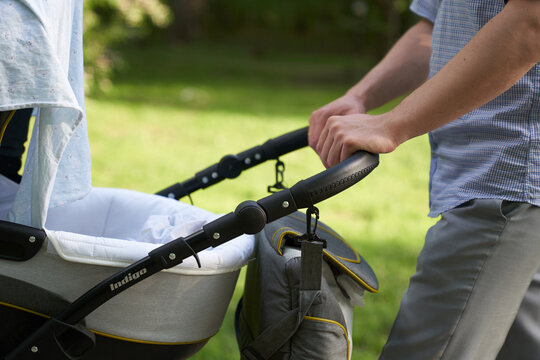 A young dad walking in the park with a baby in a stroller. Close-up of men's hands with a stroller. Father's Day concept. High quality photo