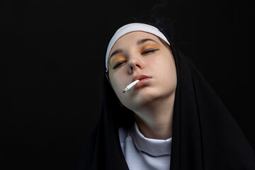 Close-up portrait of a young nun on a black background. The nun smokes a cigarette.