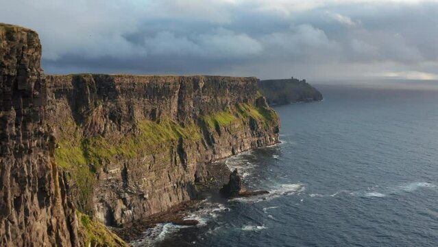 Beautiful panoramic footage of long and high cliffs at sea coast. Backwards fly along rugged rock wall above rippled water surface. Cliffs of Moher, Ireland