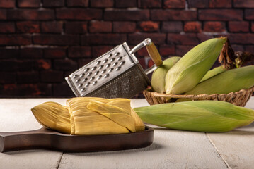 Fototapeta na wymiar Brazilian corn snack pamonha and green corn arranged on a white rustic wooden table, selective focus.