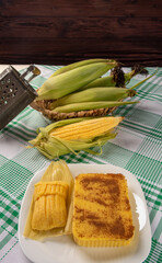 Brazilian Cural, candy corn and pamonha, corn on the cob arranged on a table with a green and white tablecloth, dark background, Selective focus.