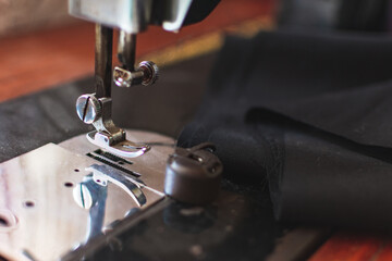 Close-up photo of sewing machine with black piece of fabric. Fashion design