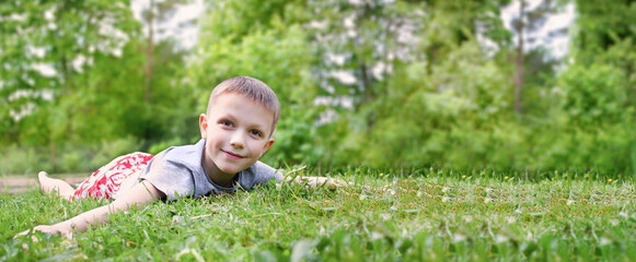 A happy child lies on a green field. The boy has fun on the grass, on a sunny day. The concept of a happy childhood, ecology and a clean planet for generations. copy space