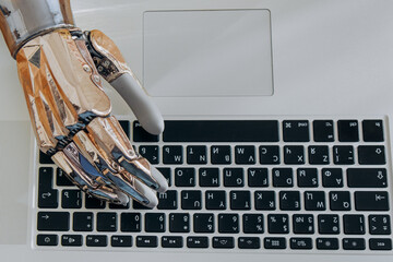 Young woman uses modern metal bionic arm to type on laptop keyboard sitting at wooden table in...