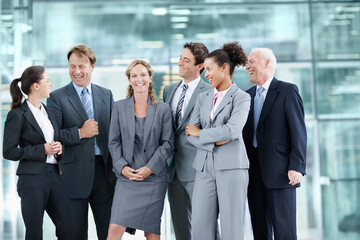 Supported by her proud team of coworkers. Positive group of businesspeople standing together and smiling while surrounding a coworker - portrait.