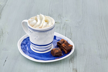 Cup of coffee with whipped cream and chopped chocolate on a light blue wooden table