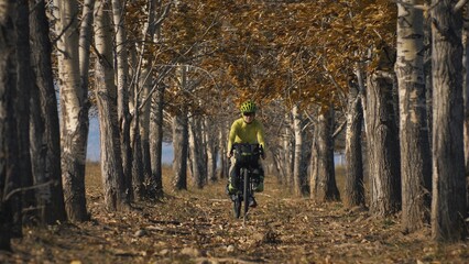 The woman travel on mixed terrain cycle touring with bikepacking. The traveler journey with bicycle bags. Sportswear in green black colors. The trip in magical autumn forest, arch, alley, avenue.