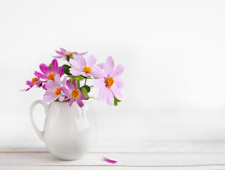 Fresh delicate pink flowers in white jar on rustic white wooden background.