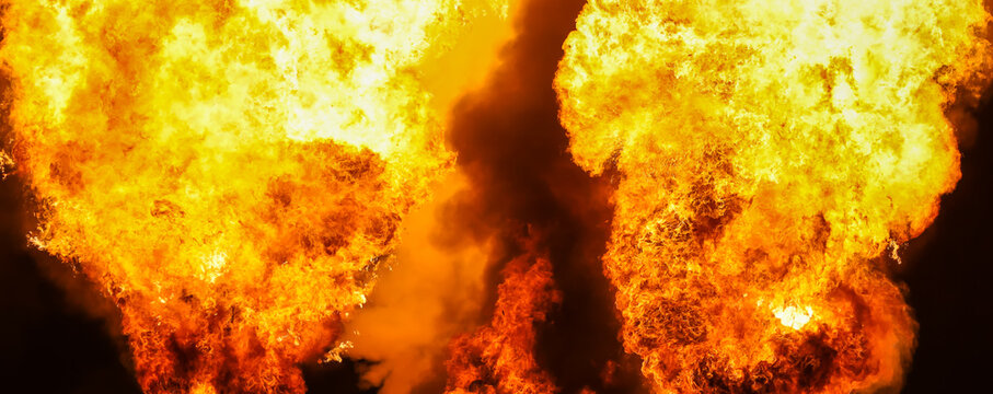 Photograph of huge flames, fire, and explosions against black night sky that can be used as fiery abstract texture, element or for a background.