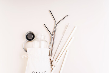 Zero waste and eco friendly,plastic free concept.Reusable glass bottle on white background.Cotton bag,glass bottle and metal reusable and paper disposable tubes.Copy space.Ecological,natural materials