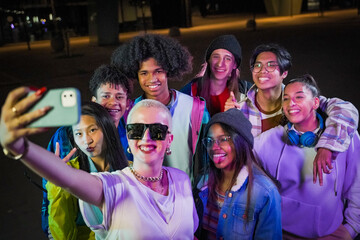 Group of young people with modern outfits taking a selfie in the street wth neon lights at night.