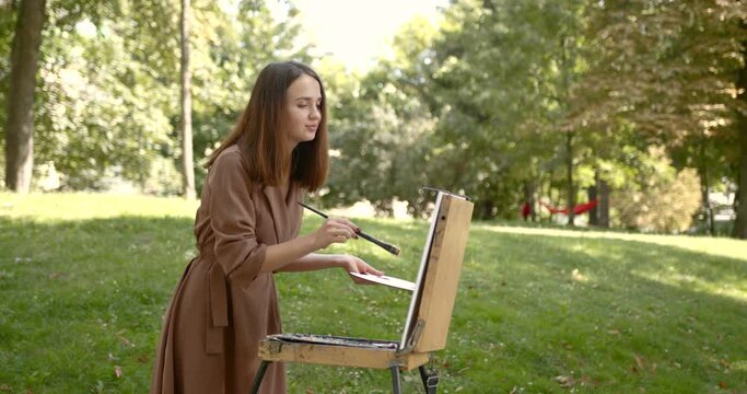 Girl artist paints on an easel in the park
