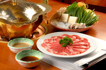 Shabu-shabu dish with vegetables, noodles, sauces, tofu and fondue burner on wooden table	