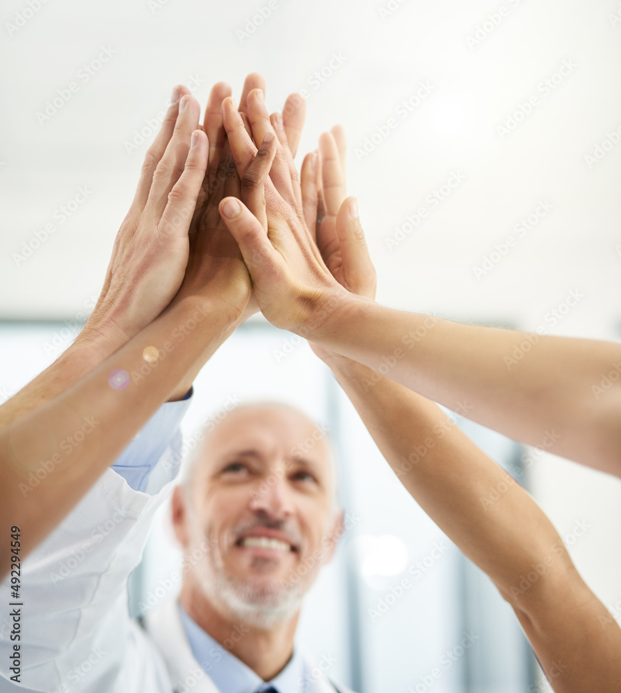 Poster United in the fight against disease. Cropped shot of a group of doctors giving each other a high five in a hospital.