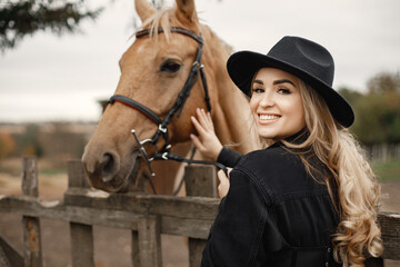 Woman touching a brown horse behinde the fence on a farm