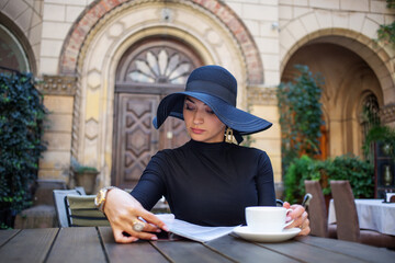 Exquisite woman in a black hat drinks coffee