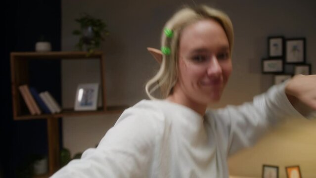 Woman recording dance video in living room. Young female student or teenager dancing at home for musical clip. Blogger making music content for channel, wearing elf ears.