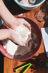 Child's hands holding flour above a bowl of play dough mix