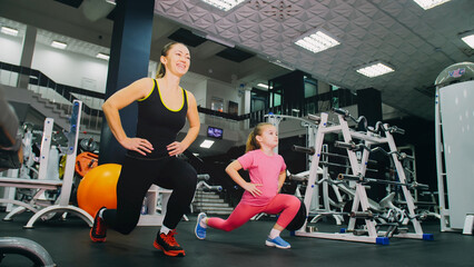 Fototapeta na wymiar Mother and Daughter in the Gym, Family Performs Physical doing Exercises Fitness, Healthy Lifestyle. Happy Sports Family Training Concept. Woman with her Child doing Stretching Warm-up in the Gym