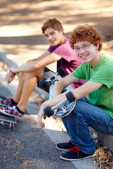 This beats sitting around indoors. Portrait of two young skateboarders sitting beside a road.