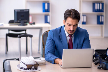 Young male employee preparing for trip at workplace