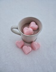 Mug of hot chocolate with heart-shaped marshmallows on bed of snow