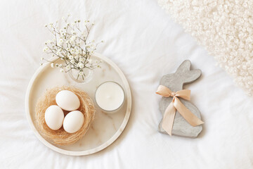 Fototapeta na wymiar Marble tray, nest with white eggs, decorative bunny figure, candle and gypsophila flowers on a white background. Easter decor. Flat lay, top view.