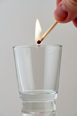 Hand holds a burning match over a transparent glass - 492309941