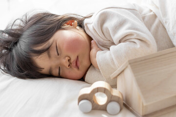 Obraz na płótnie Canvas 昼寝している赤ちゃんと、オモチャの家と車(1歳8ヶ月、日本人、女の子)。子供との生活設計のイメージ