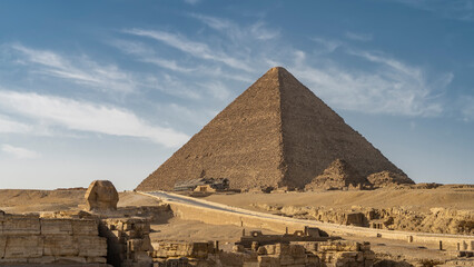 The pyramid of Mycerinus on the background of the blue sky. Nearby are the pyramids of queens. The highway passes through the desert. In the foreground are the ruins of the temple of the Sphinx. Egypt - obrazy, fototapety, plakaty