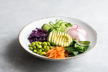 Buddha bowl with avocado, edamame beans, cucumber, red cabbage, carrots, radishes and spinach. Vegetable salad.
