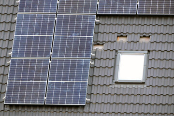 Solar panels being installed on an anthracite roof of a house next to a roof window