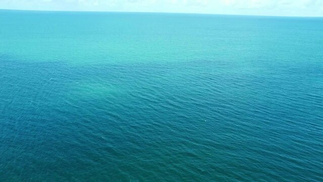 Aerial video of blue ocean panning up to show blue sky