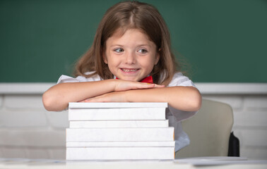 Smiling girl sitting at the desk and holding hands on the books in the school classroom. First day at school.
