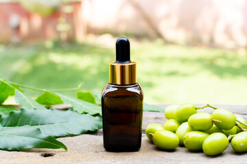 Neem oil in glass bottle with neem fruit and green leaf on wooden and blur background on sunny day.