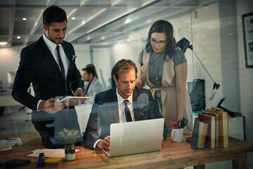 Increasing productivity with teamwork and extra hours. Shot of a team of colleagues using a laptop...