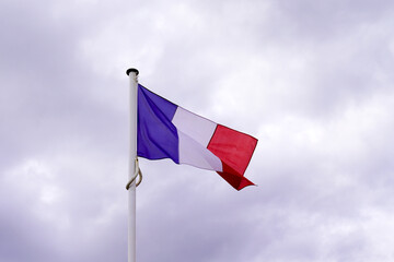 French tricolors blue white red flag waving front on cloudy sky in town of france