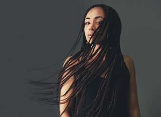 Braids in the breeze. Studio portrait of a beautiful young woman posing against a gray background.