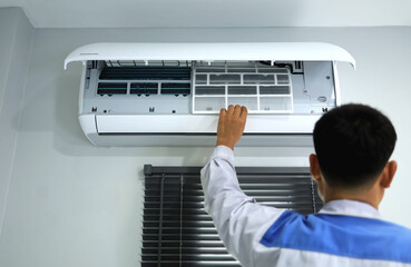 The air conditioner technician is putting the air filter back into the indoor unit air conditioner after cleaning it.