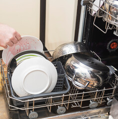 A man loads dirty dishes, plates, spoons, forks, cutlery into the dishwasher tray