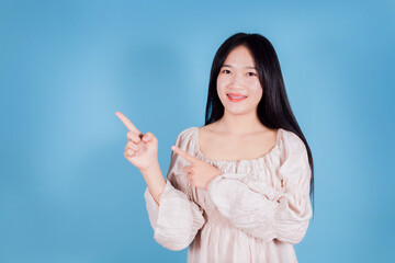 Portrait of smiling asian woman pointing finger to the side on blue background