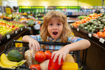 Child in the supermarket. Funny excited little boy wit shopping cart choosing goods at grocery store or supermarket. Shopping cart, grocery store concept.