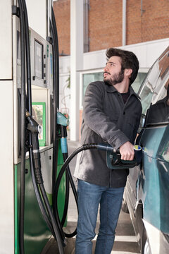 Young Man Refueling His Vehicle With Gasoline While Looking At The Prices At A Gas Station.