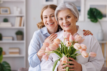 Young woman congratulations elderly mother with bouquet of fresh tulips