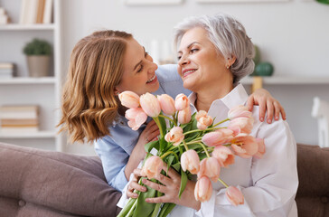 Young woman congratulations elderly mother with bouquet of fresh tulips